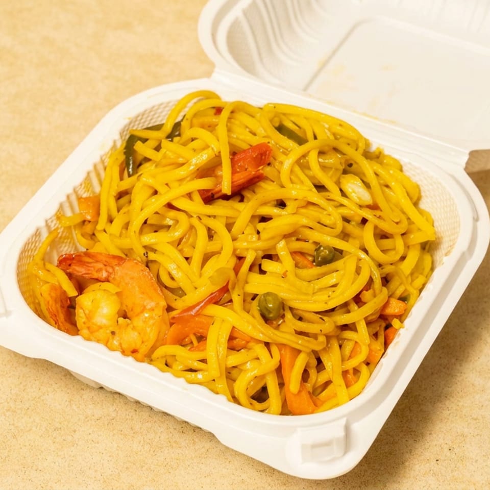 Takeout container filled with yellow noodles, shrimp, carrots, peas, and red pepper slices on a wooden table.